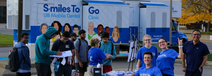 A crowd gathers before a table in front of the Mobile Dental Unit. 