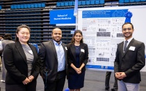 Four student researchers in blazers in front of a research poster. 