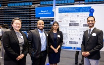 Four student researchers wearing blazers pose alongside a research poster. 