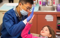 A dentist and pediatric patient high five each other. 