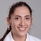 Smiling resident in a white coat in front of a gray back drop. 