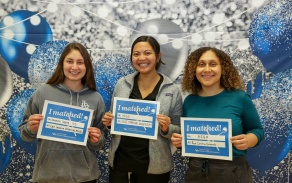 Three dental students in front of a background holding up Match Day signs. 