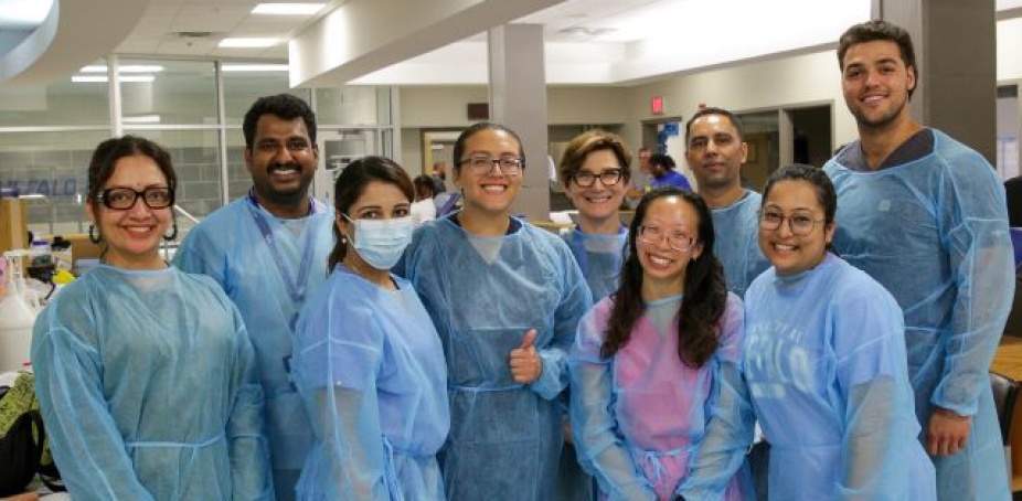 DDS Students in scrubs and dental gear taking a group photo in the University at Buffalo Sports trainer's room. 
