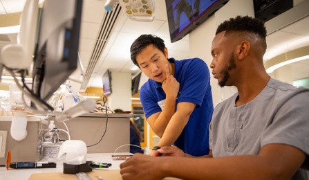 Two dental students wearing scrubs working on a table bench in our pre clinical simulation center. 