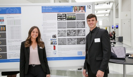 Two dental students standing in front of posters on easels that show a visualization of their research. 