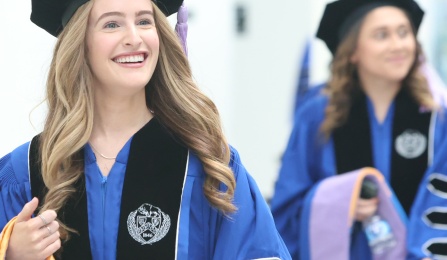 Dental student at commencement in graduation regalia walking in a large hallway. 