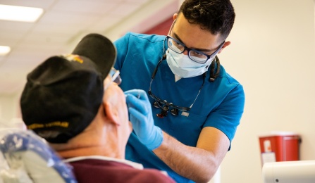 A dental student in scrubs and mask working on a patient in our clinical area. 