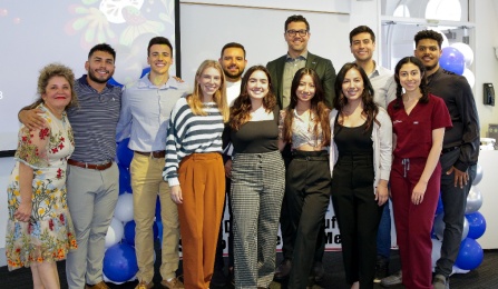 Photo of dental students, Dean, and faculty standing in front of a presentation. 