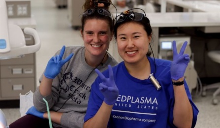 Two dental students sitting down and waving in our pre clinical simulation center. 