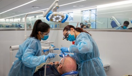 dental students in scrubs and mask working on a patient in our clinical area. 