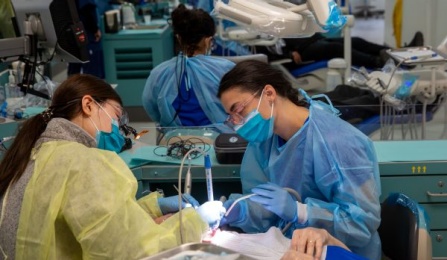 two students in masks and scrubs working on a patient in our clinic area. 