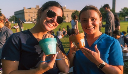 Two dental students outside holding up pottery with teeth on them. 