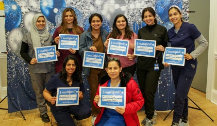 A group of dental students standing and kneeling in front of a celebratory background holding up signs of where they have matched for residency programs. 