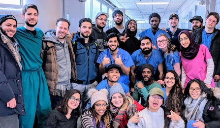 a group of students wearing scrubs outside of Gross Lab standing and kneeling. 