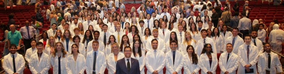 Group of students attending a ceremony wearing white coats. Dean is in the front of the group. 