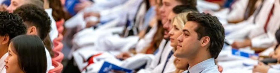 Group of students attending a ceremony wearing white coats. 