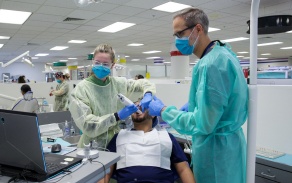 A student and faculty wearing PPE use an intraoral scanner on another student as part of a class demonstration. 