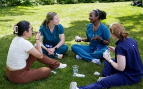 Four dental students sit in a circle outside and have lunch. 