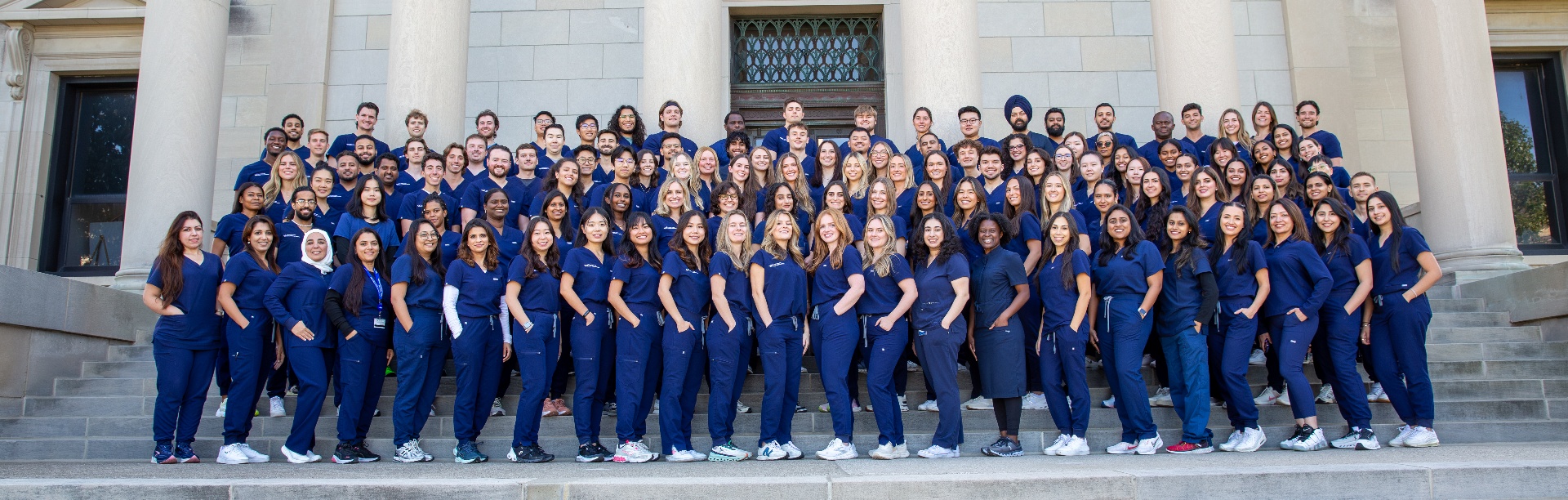 Class of 2027 in blue scrubs on the steps of Squire Hall. 