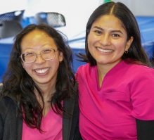 Two students wearing scurbs sitting behind a table. 