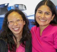 Two UB SDM students wearing scurbs sitting behind a table. 