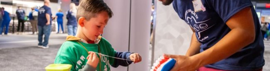 dental student showing a young child how to floss on a big set of teeth. 