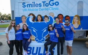 Six students standing in front of our dental mobile unit holding up their hands in blue shirts. 