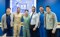 Photo of seven dental students wearing scrubs standing in front of a powerpoint presentation in classroom. 