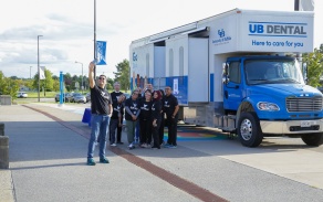 dental students, staff and SDM Dean take a picture in front of the UB mobile dental clinic. 