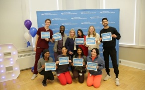 dental students standing and kneeling holding up match day signs in front of a large banner. 