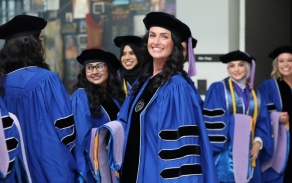 dental student in graduation robe standing in large hallway. 