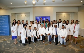 group photo of dental international dental students in white lab coats standing and kneeling in hallway. 