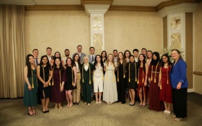 students posing with faculty members in front of a large wall. 