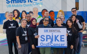 Students and staff in front of the UB mobile dental clinic holding a sign for the Spike Oral Cancer event. 