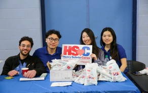 4 Students at a table and one is holding a sign for Henry Schein Cares at the UB Dental Day at the Belle Center 2025. 
