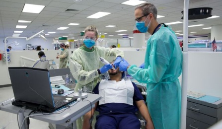 faculty member with one student doing a dental scan on another student in the clinic. 