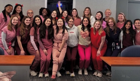 group of dental students in pink scurbs huddled together in classroom. 