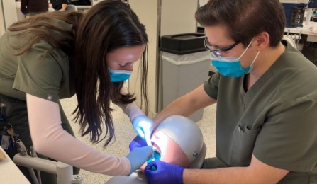 two dental students in scrubs working on a mannequin in the preclinic simulation lab.