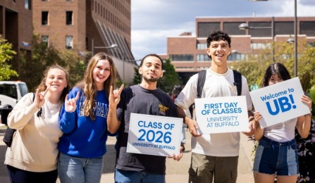 students holding up signs during their first day of school in front of academic buildings. 