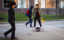 a student skateboarding on the sidewalk. 