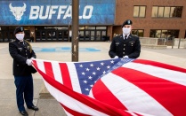 2 service men raising a flag in front of alumni arena. 