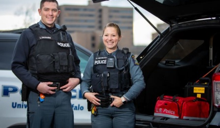 two university police officers standing in front of a police vehicle. 
