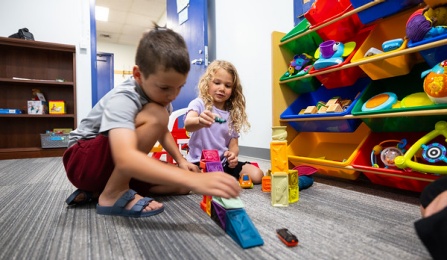 Two school aged kids playing on the floor. 