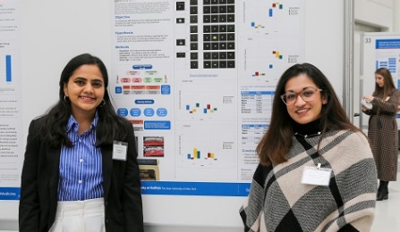 Two dental students standing in front of their poster presentation in a large loby hall. 