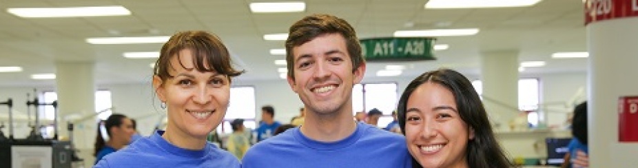 Photo of three students standing and smiling in clinic wearing University at Buffalo Bulls shirts. 
