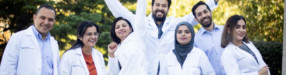 Photo of several dental students wearing white laboratory coats standing in front of trees. 