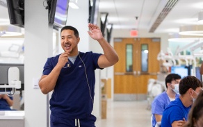 A dental instructor in scrubs talking to a class. 