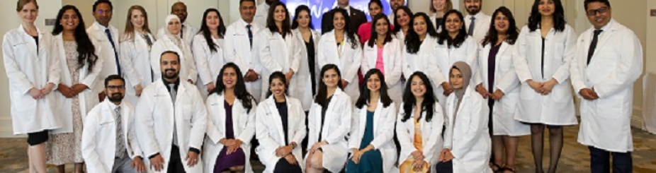 International Dentist Program students standing and kneeling in their white lab coats for a group photo. 