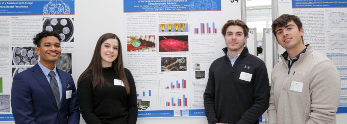 Four students pose with research posters. 