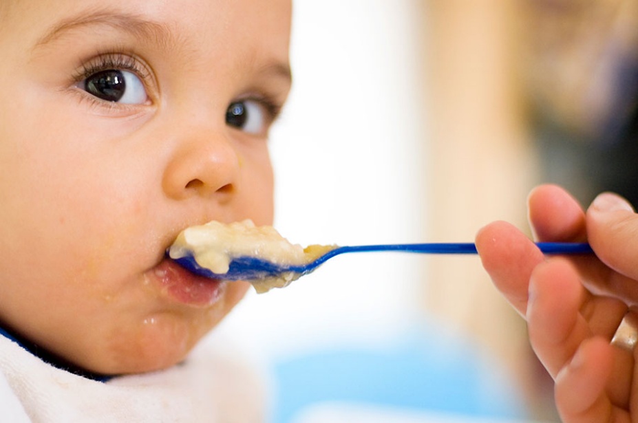 Baby being fed an oatmeal-like cereal with a spoon.
